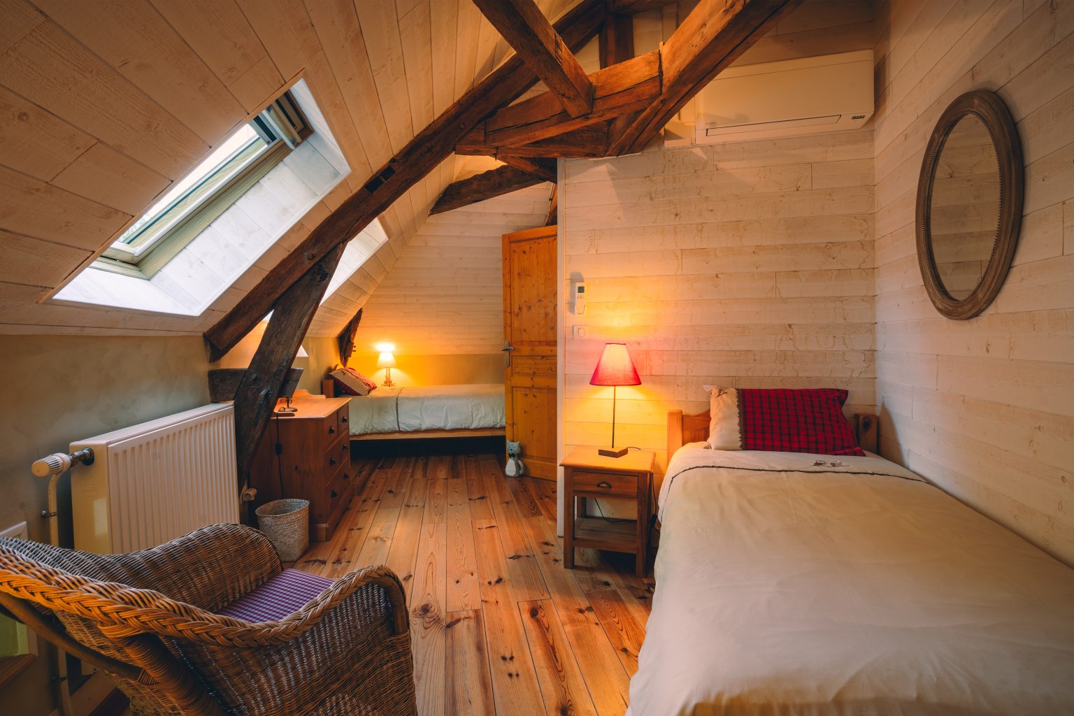 Chambre mansardee avec miroir rond et fauteuil en osier