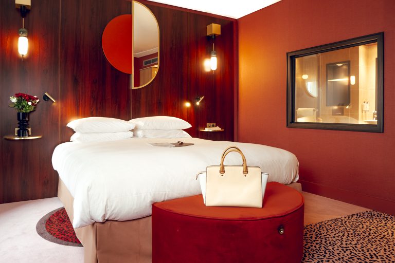 Chambre d'hôtel cinq étoiles, lit et pouf devant un mur laqué rouge