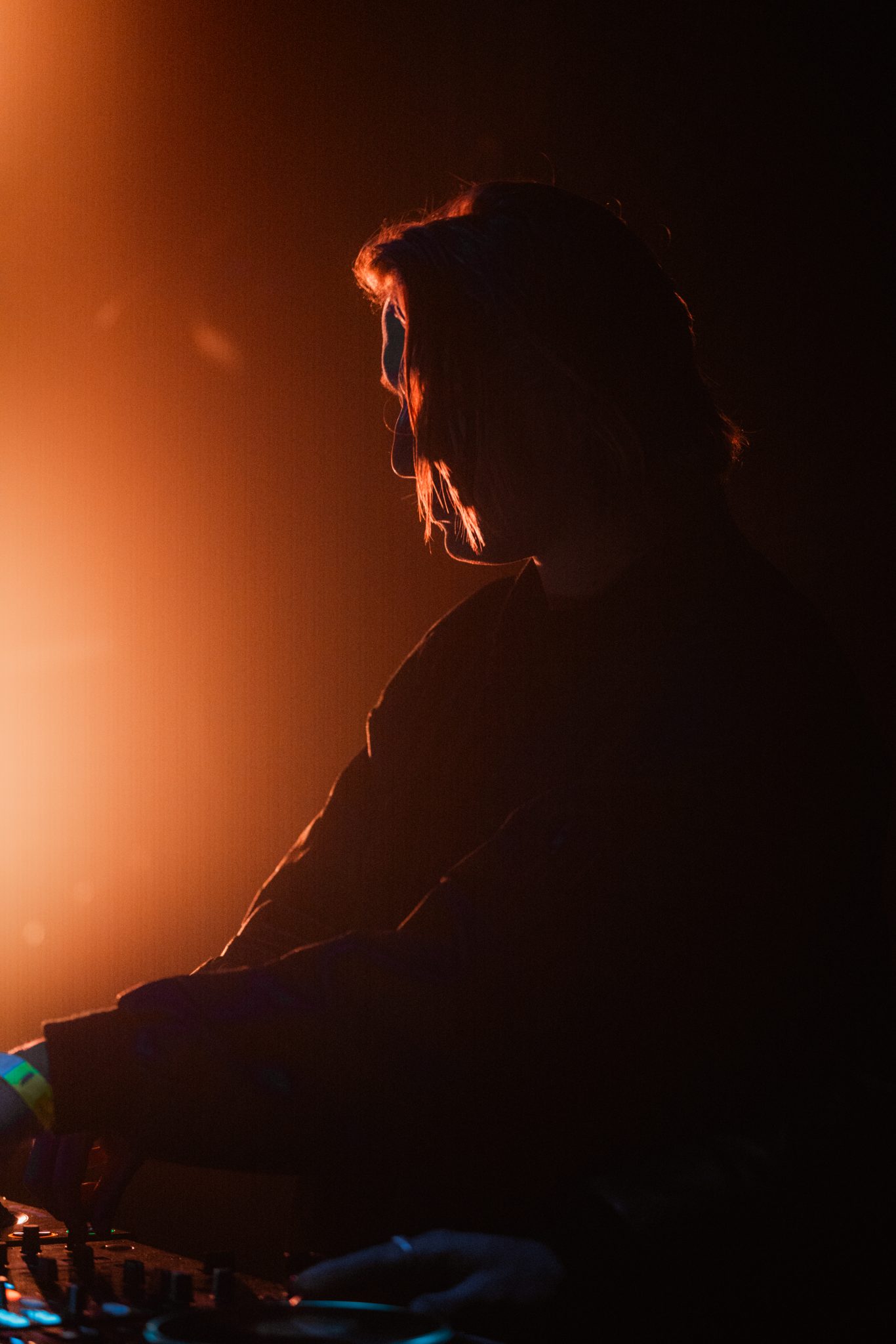 DJ en silhouette aux platines, lumiere chaude