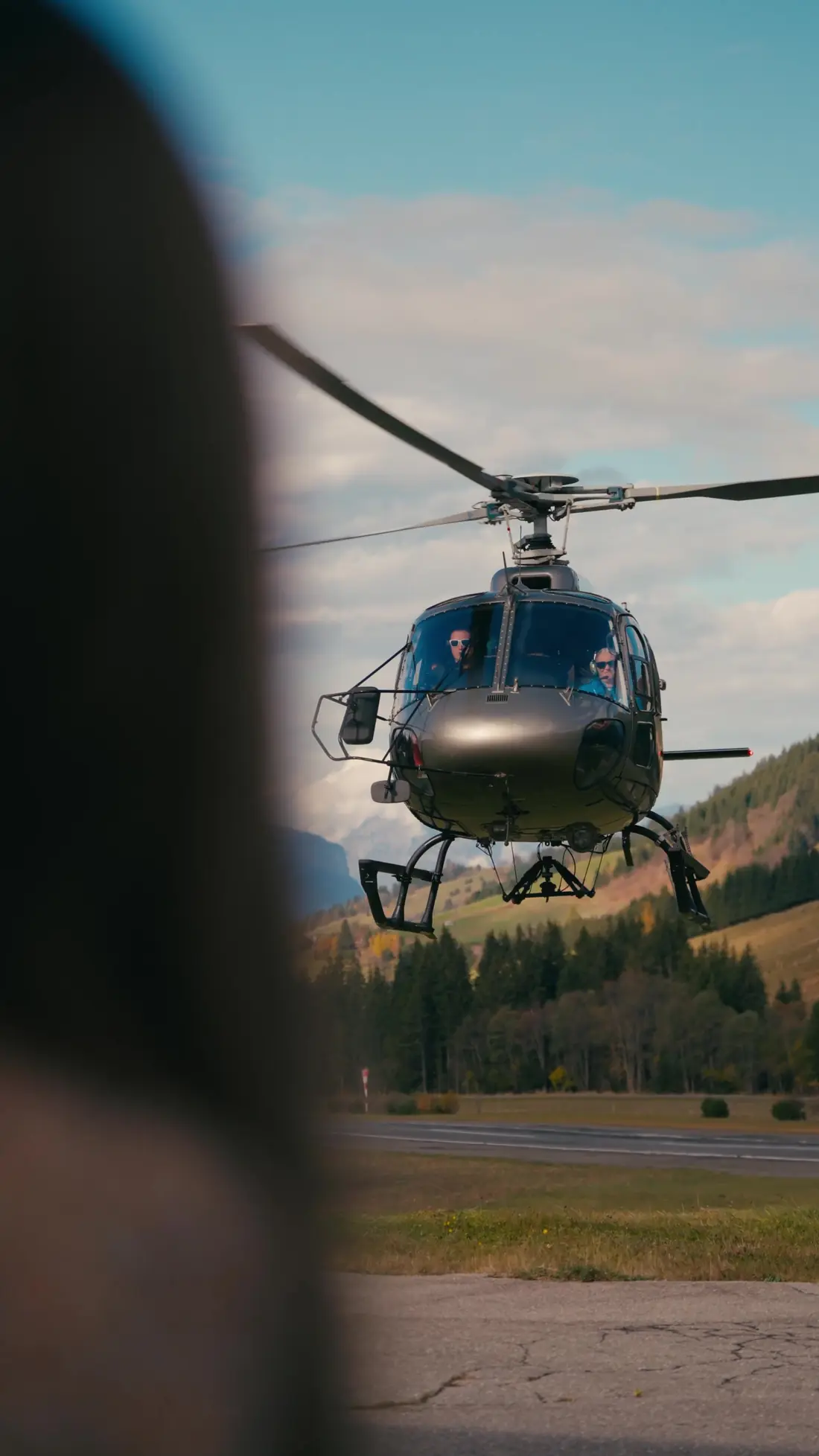 Hélicoptère en approche au-dessus de la piste de l'altiport de Megève, forêts d'automne derrière