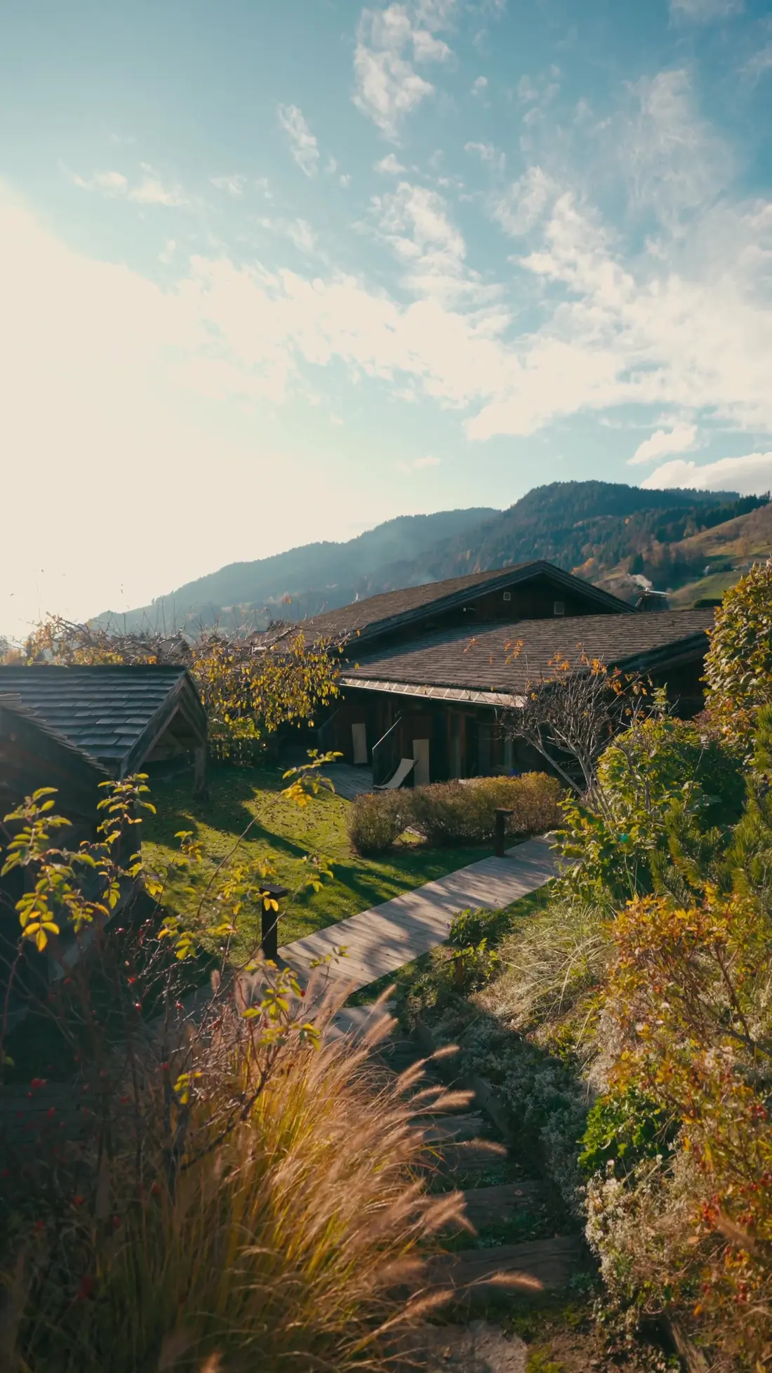 Chalet en bois et lauzes au-dessus d'un jardin d'automne, alpages et crêtes en arrière-plan à Megève