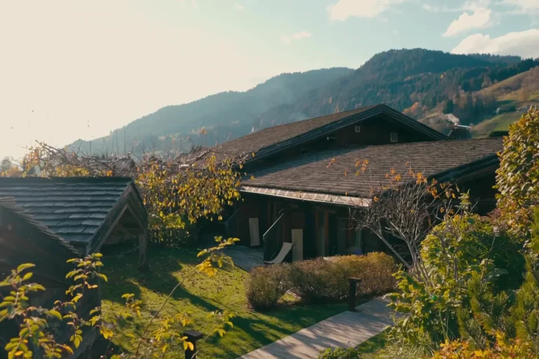 Chalet en bois et lauzes entouré d'un jardin d'automne, alpages et sommets en arrière-plan