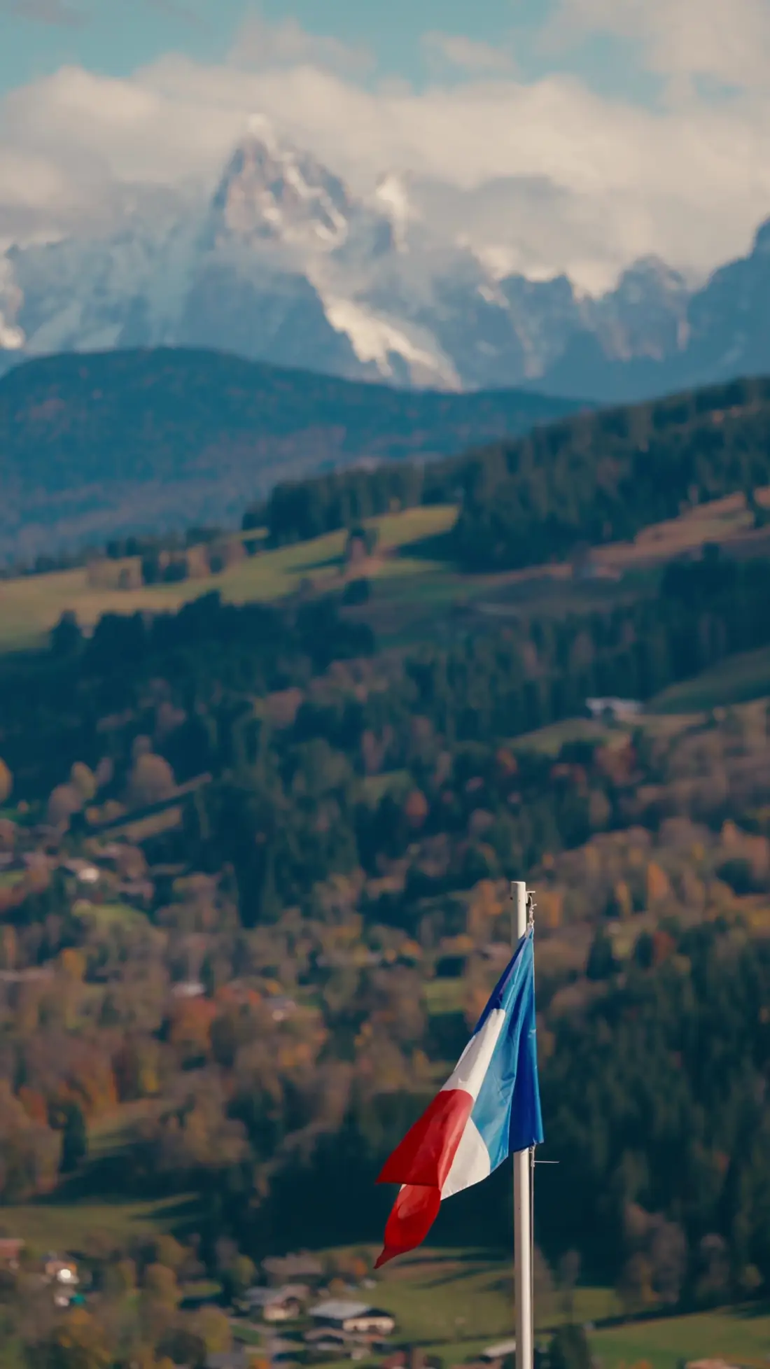 Drapeau français au-dessus des alpages et des forêts d'automne, sommets enneigés du massif du Mont-Blanc en arrière-plan, vus depuis Megève