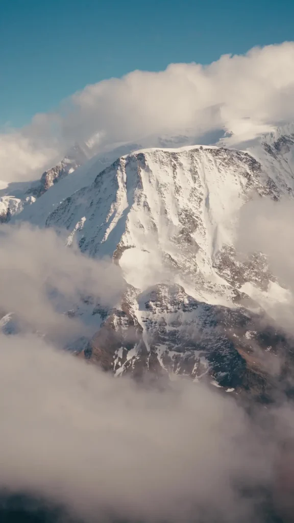 Face enneigée du massif du Mont-Blanc émergeant des nuages, vue d'hélicoptère