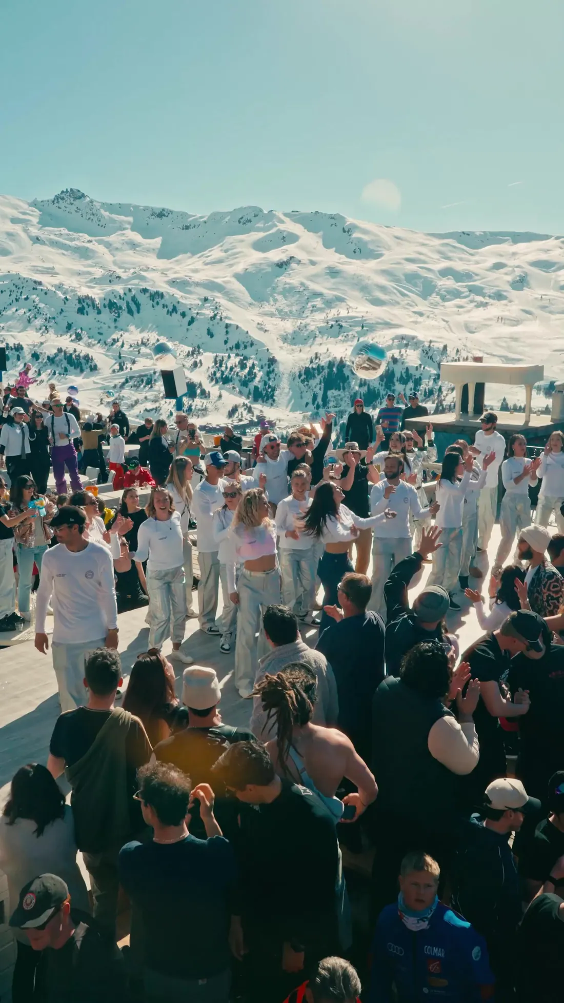 Troupe de danseurs vêtus de blanc au milieu du public, massif enneigé de Méribel en arrière-plan