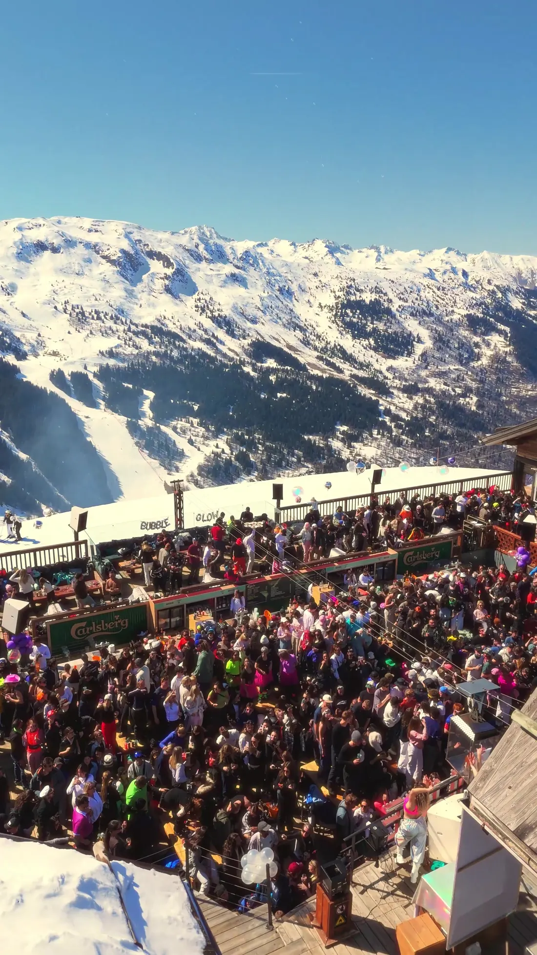 Foule sur la terrasse de la Folie Douce, versants enneigés et pistes de la vallée de Méribel en face