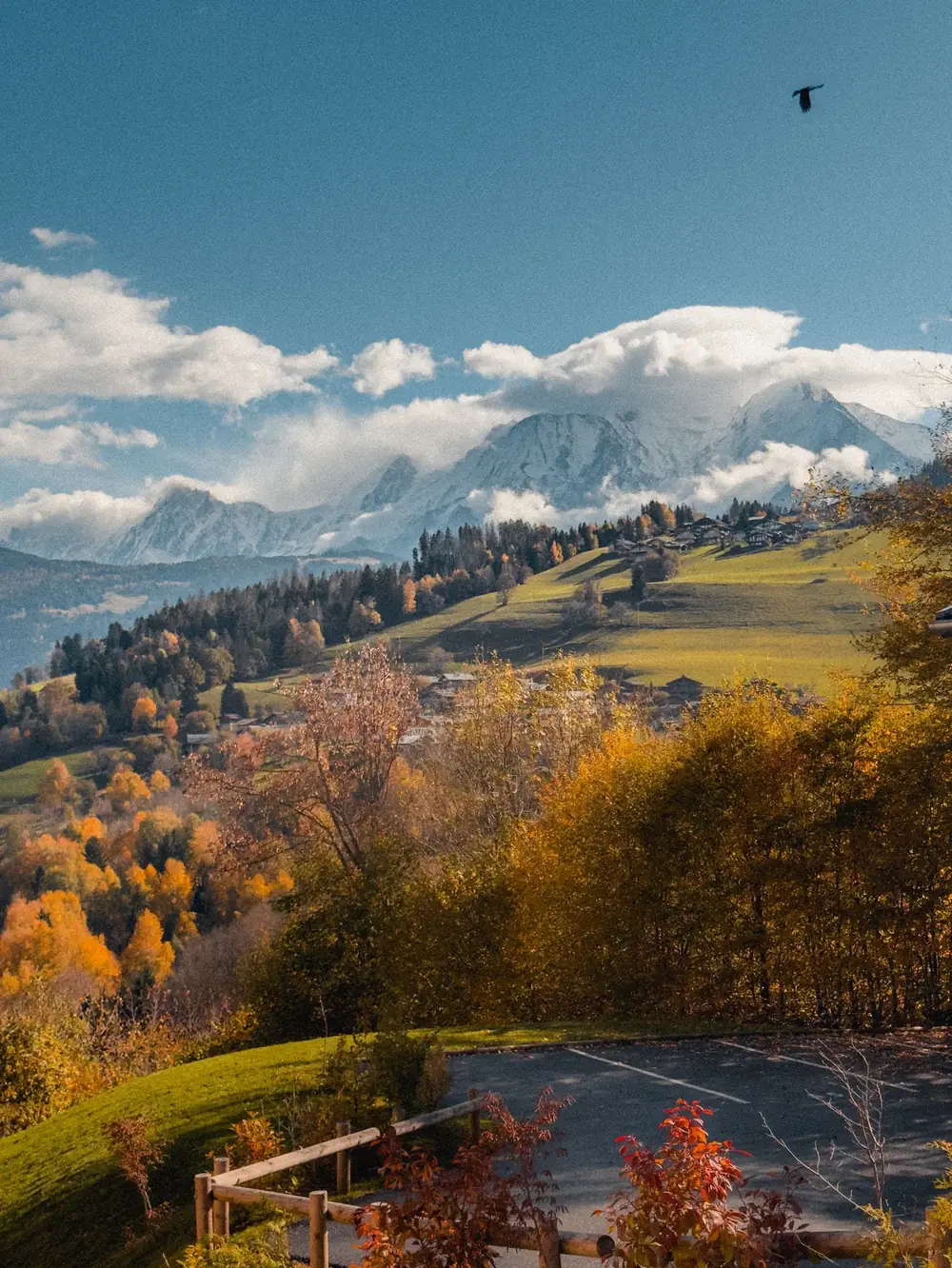 Fin d'automne en montagne, arbres dorés, chalets sur les pentes et sommets enneigés dans les nuages