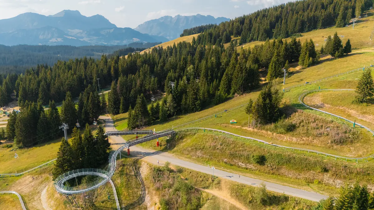 Vue aérienne de la piste de luge sur rail serpentant entre les alpages et les sapins des Saisies