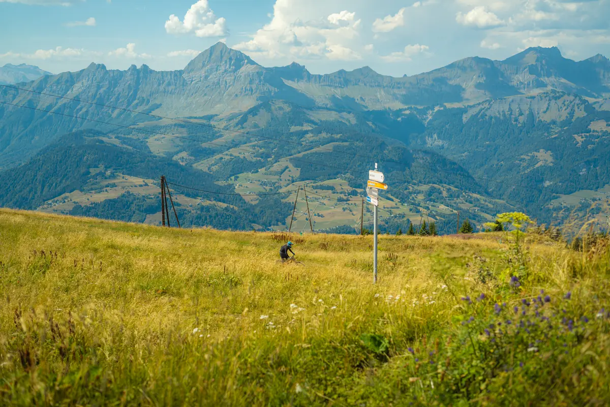 Alpage et poteau directionnel au premier plan, chaîne des Aravis en enfilade sous un ciel dégagé