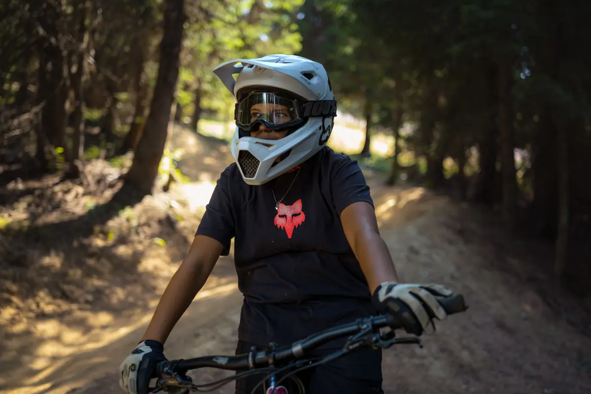 Portrait d'une vététiste casque intégral relevé, sentier de forêt en arrière-plan