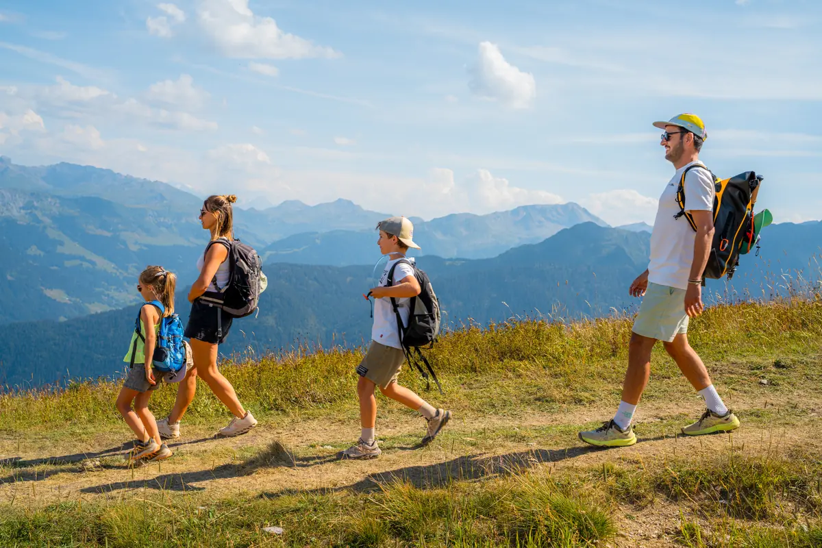 Famille en file sur un sentier de crête herbeux, vallées et sommets dans la brume de chaleur