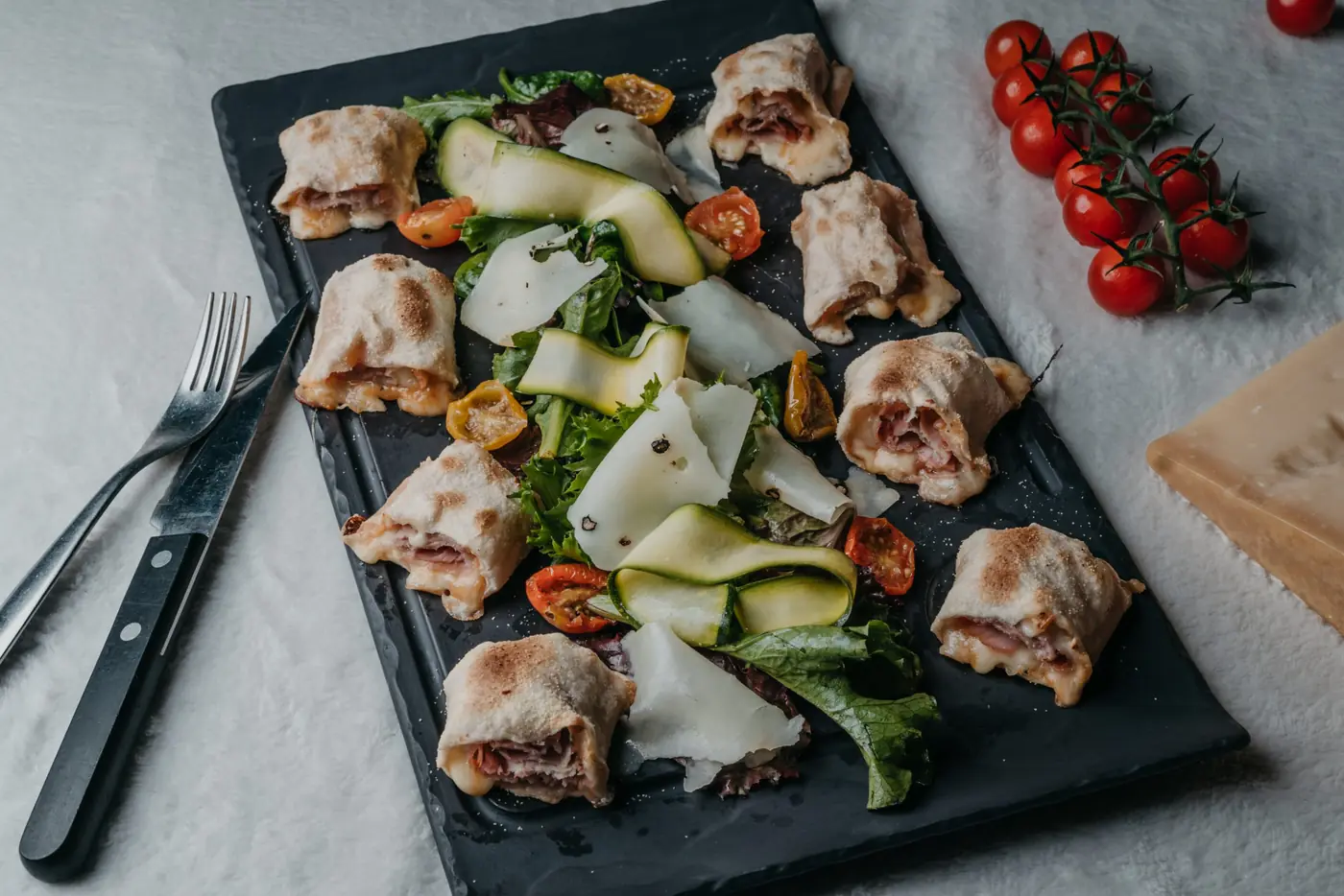 Feuilletés garnis et lamelles de courgette servis sur une ardoise, nappe blanche