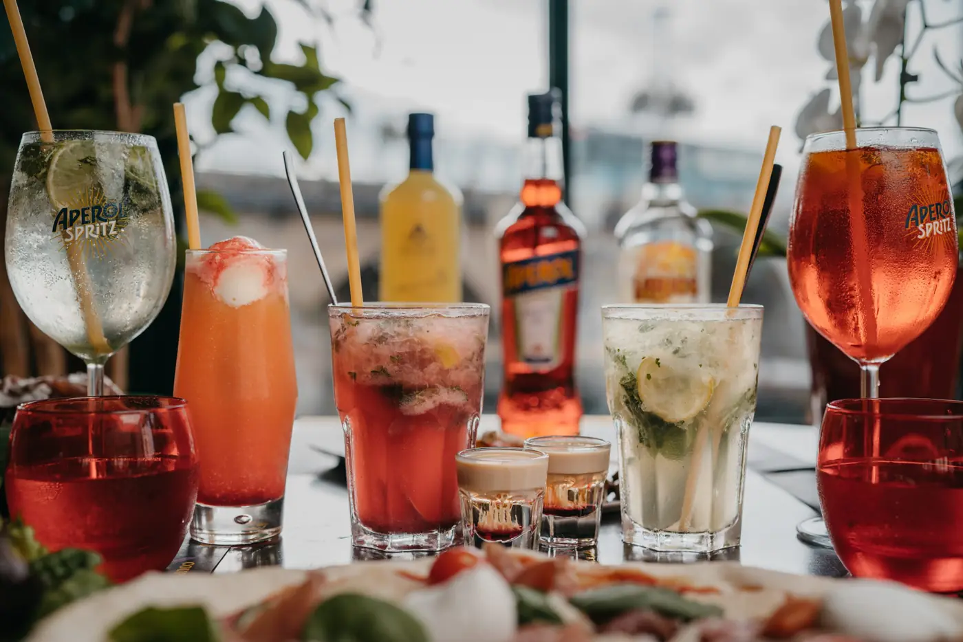 Cocktails colorés alignés sur la table, bouteilles d'apéritif derrière