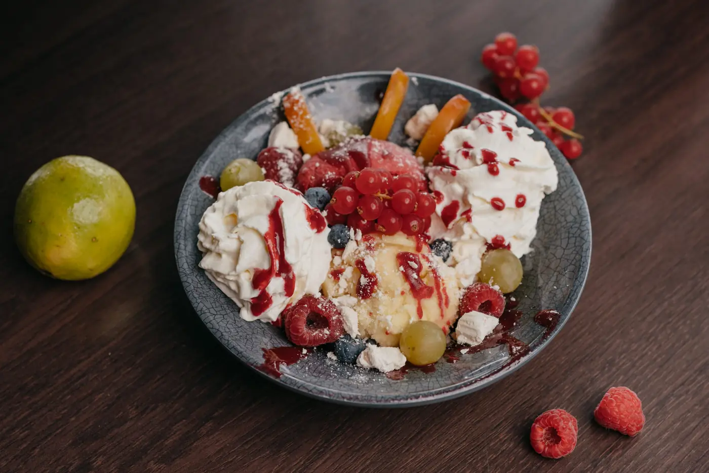 Coupe glacée aux fruits rouges et chantilly, framboises et agrume posés sur la table en bois