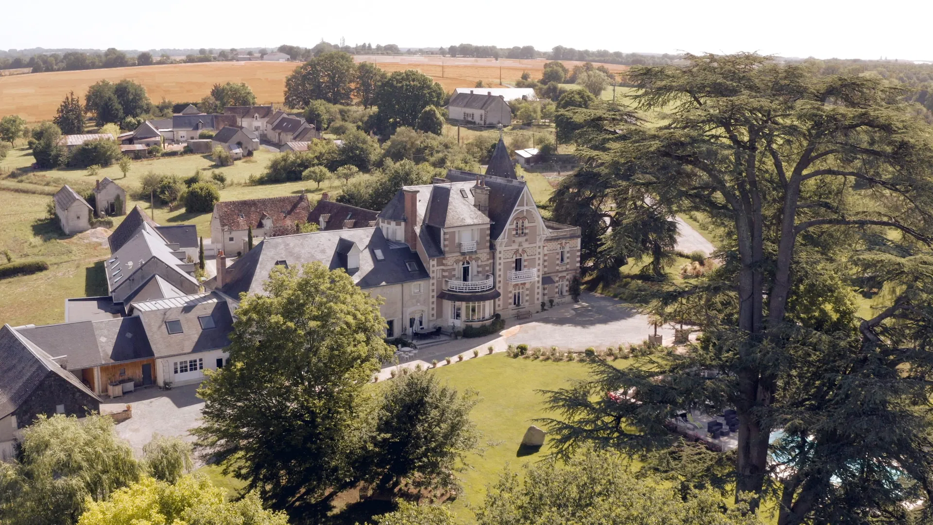Vue aérienne du Domaine de la Poignardière, demeure en pierre et ardoise au milieu de son parc arboré, champs à l'horizon
