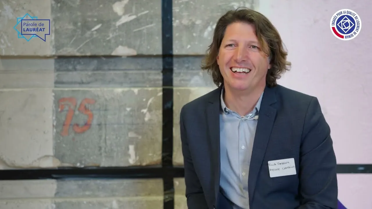 Un lauréat du programme EQLD sourit pendant son interview, mur de pierre et logos du programme à l'image
