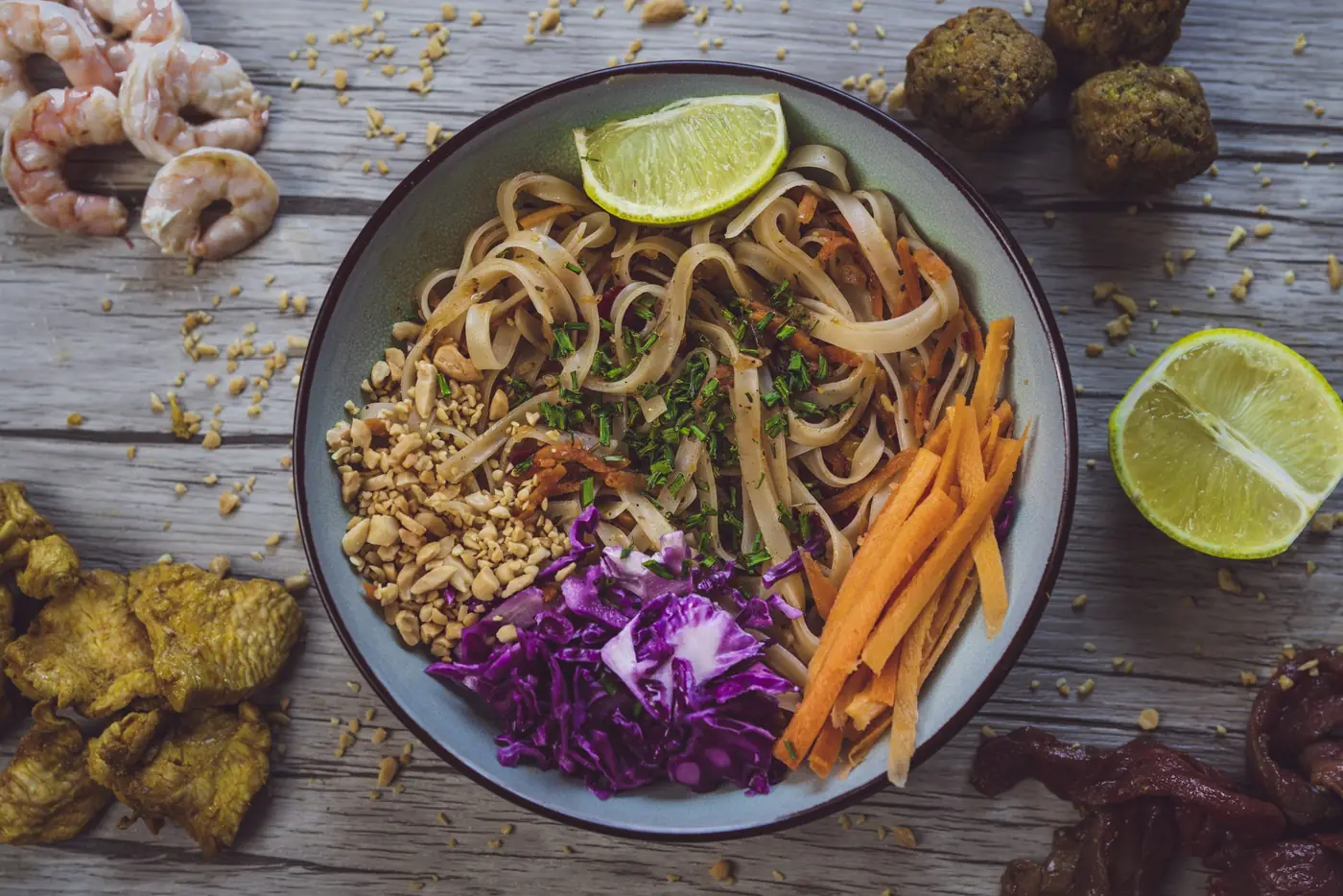 Bowl de nouilles sautées, chou rouge et carottes, crevettes et citron vert disposés autour de l'assiette