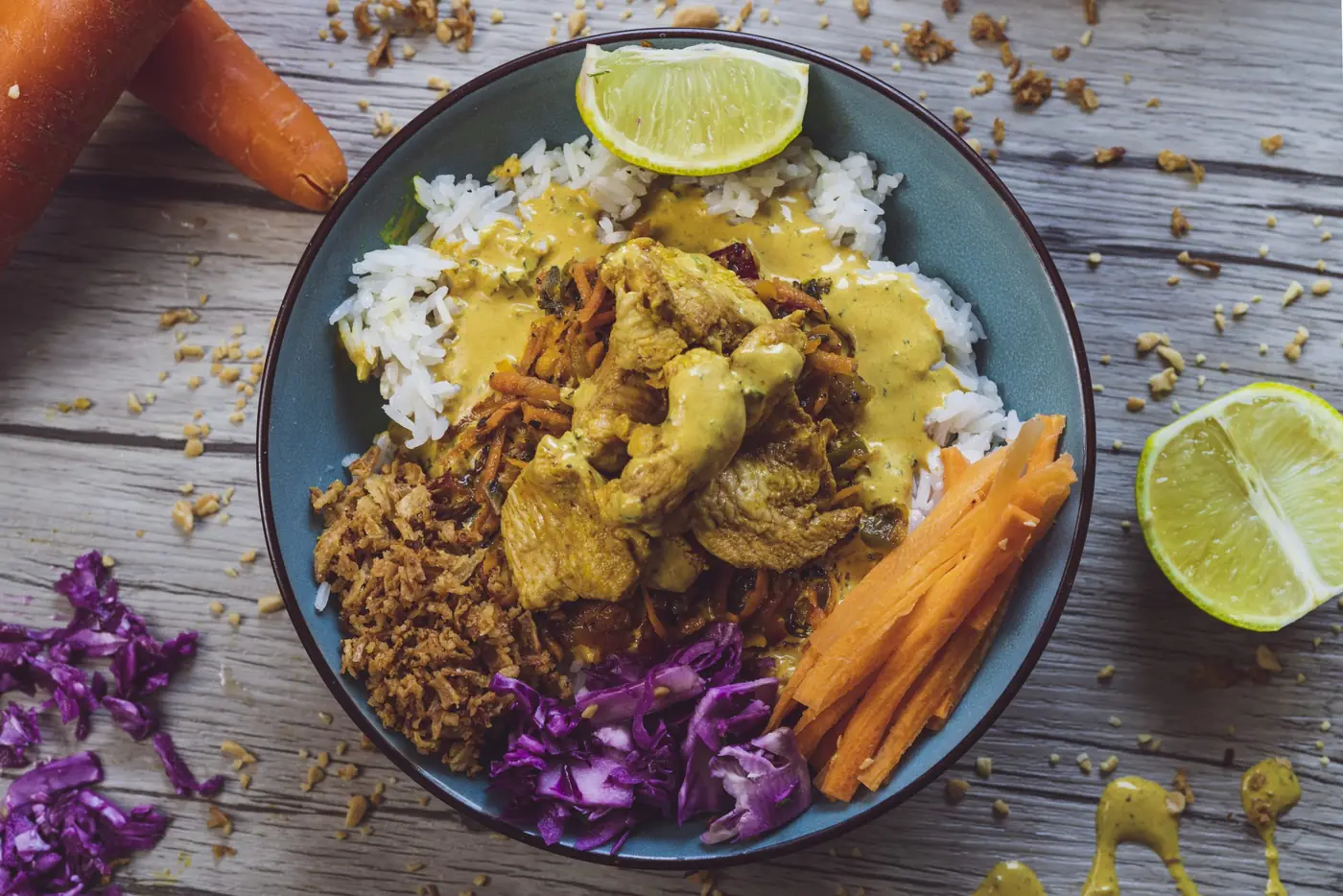 Bowl de riz au poulet curry, chou rouge et carottes, quartier de citron vert