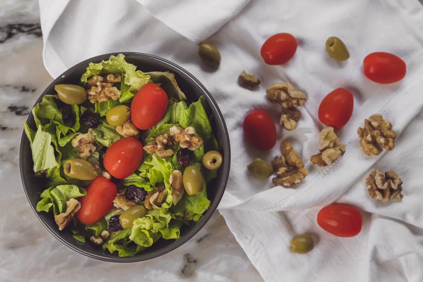 Salade verte, tomates cerises, olives et cerneaux de noix sur une nappe blanche