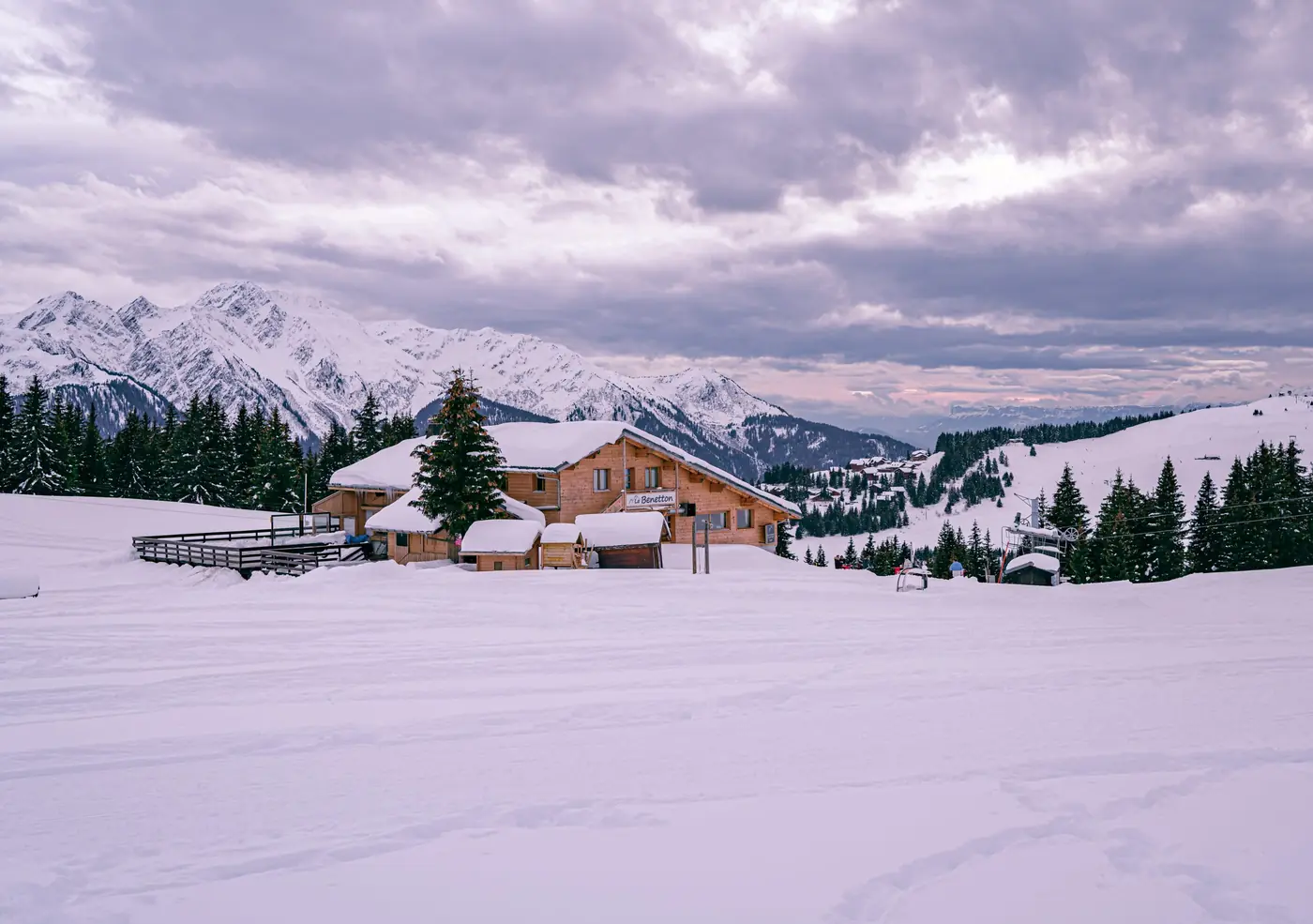 Chalet en bois isolé au milieu d'une vaste étendue de neige, sommets enneigés à l'horizon, janvier