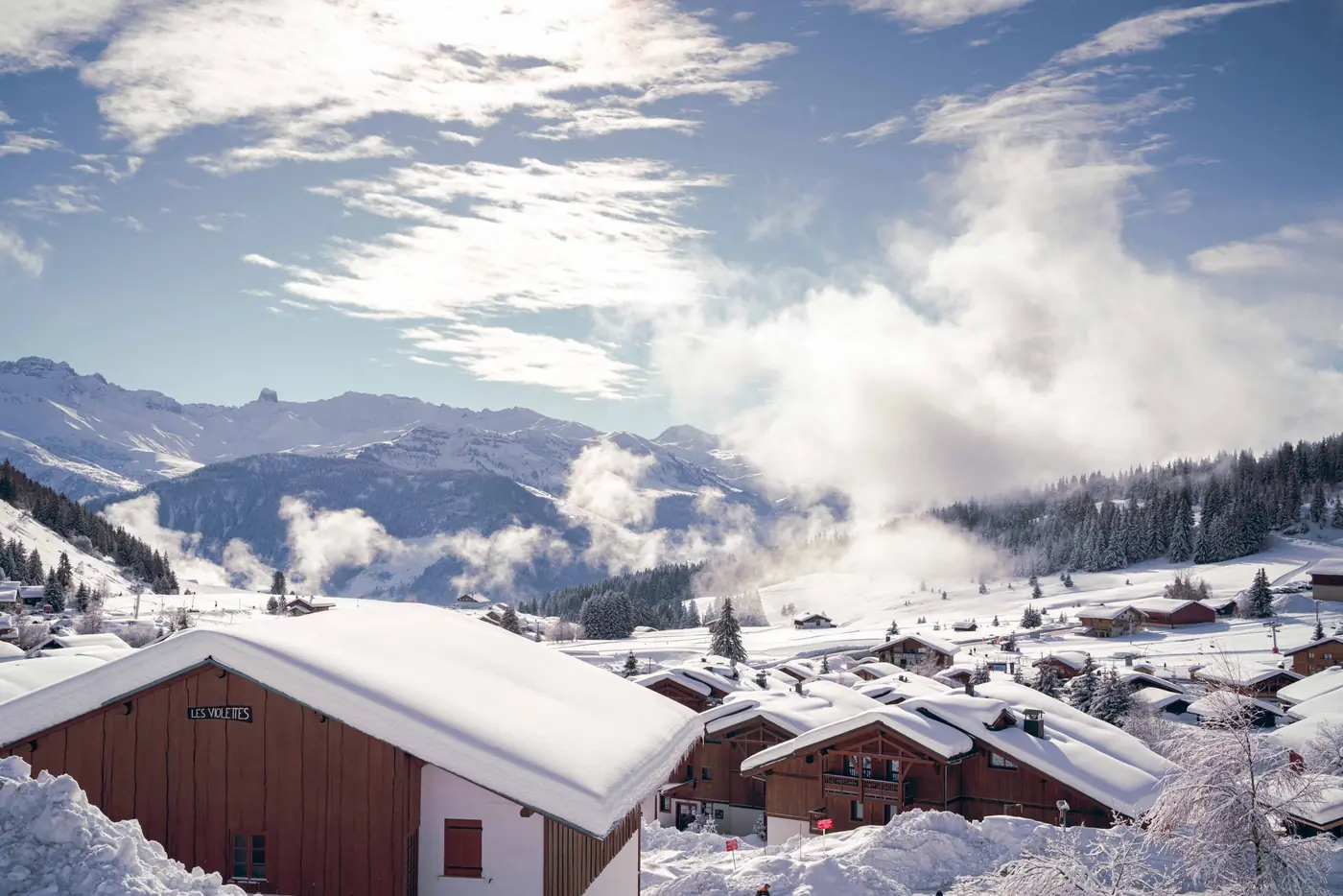Éclaircie sur les chalets enneigés du col des Saisies, nuages qui se lèvent sur les sommets