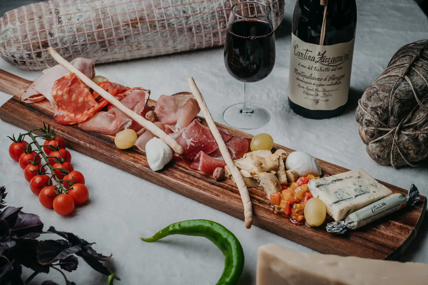 Planche de charcuteries et de fromages italiens avec gressins, piment et verre de vin rouge