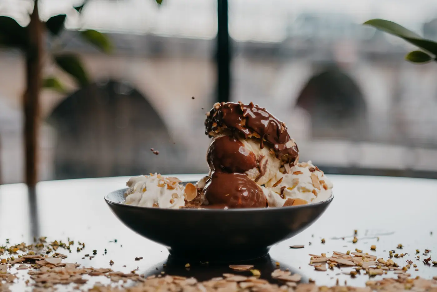 Profiteroles nappées de chocolat, pont de pierre flou derrière la baie vitrée