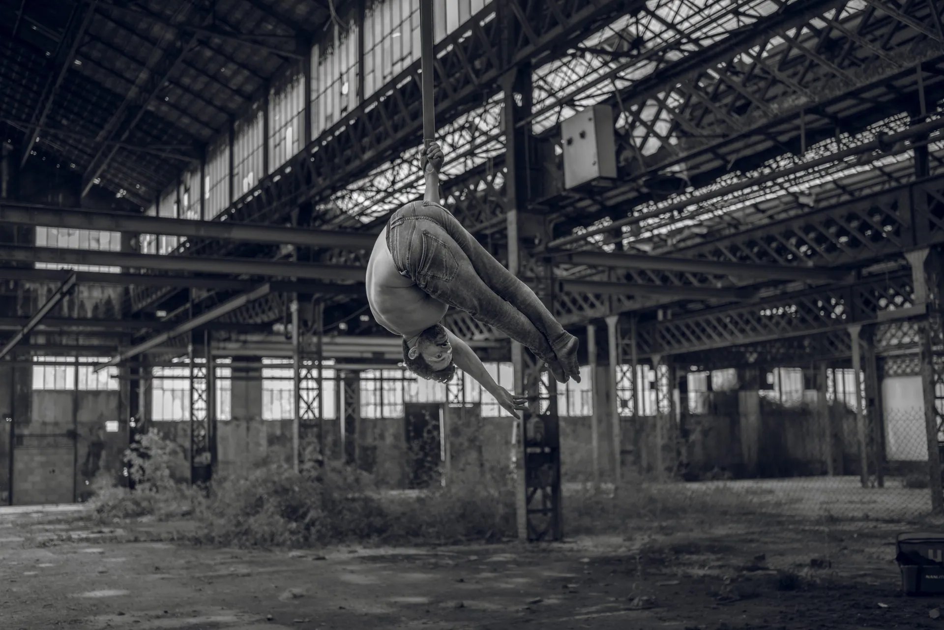 Artiste aérien en figure inversée, suspendu aux sangles au milieu d'une immense halle industrielle désaffectée à Vierzon