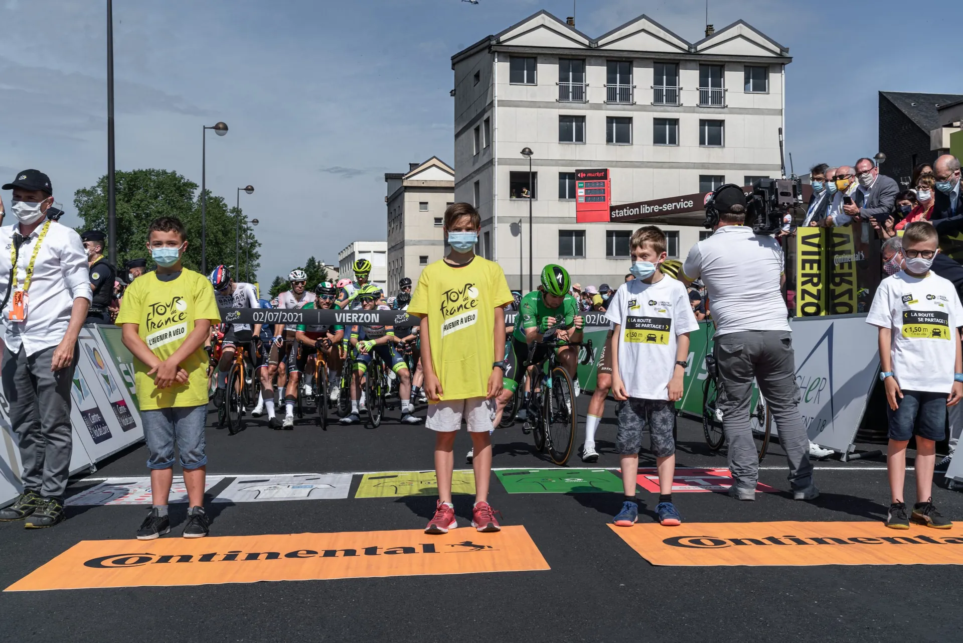 Enfants en t-shirt jaune du Tour sur la ligne de départ, coureurs derrière eux, centre-ville de Vierzon