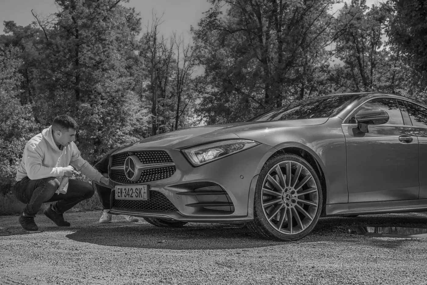 Photo de tournage en noir et blanc : un homme accroupi près de la calandre de la Mercedes CLS