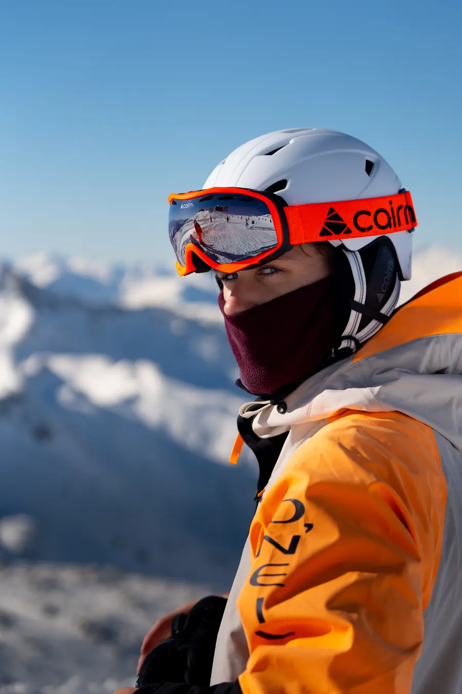 Skieur casqué au masque orange et cagoule, de profil devant les montagnes de Val Thorens