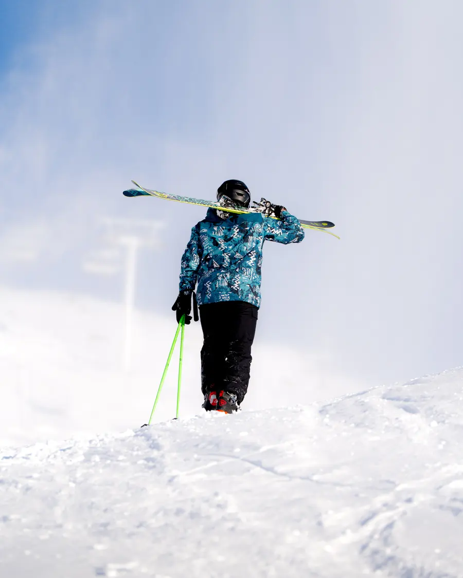 Skieur vu de dos, skis sur l'épaule et bâtons verts, au sommet d'une pente enneigée de Val Thorens